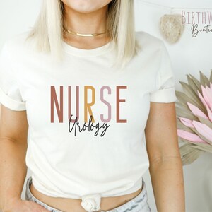 May include: White t-shirt with the text "NURSE" in brown, pink, and yellow, with the word "Urology" written in cursive underneath.