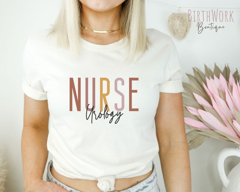 May include: White t-shirt with the text "NURSE" in brown, pink, and yellow, with the word "Urology" written in cursive underneath.