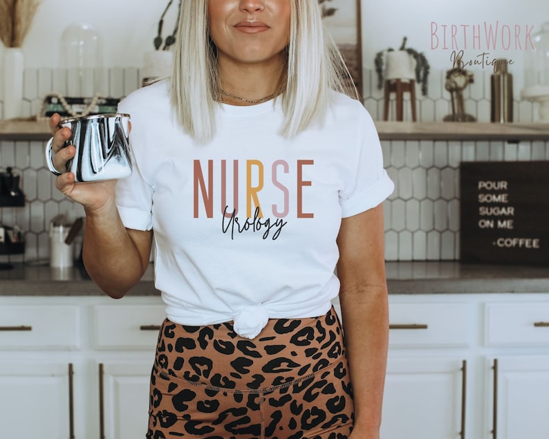 May include: White t-shirt with the text "NURSE Urology" in pink, yellow, and orange lettering. The shirt is being worn by a person with brown hair and a leopard print skirt.