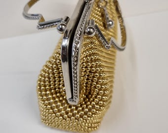 May include: A gold beaded purse with a silver clasp and handle. The purse is made of small, round beads that are woven together to create a mesh-like fabric.