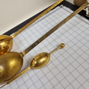Op de afbeelding: Een verzameling antieke messing meetinstrumenten, waaronder verschillende met een ovaalvormige bol en een liniaalachtige meetarm. De instrumenten zijn gerangschikt op een wit rasteroppervlak. Het messing heeft een warme, gouden tint. De metingen zijn in centimeters.