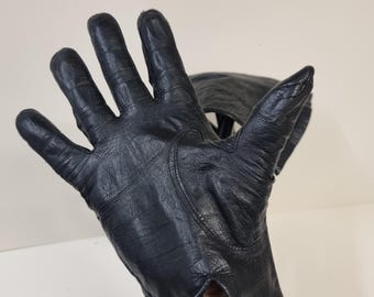 May include: A black leather driving glove with a stitched design on the back of the hand.