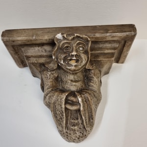 Könnte beinhalten: Eine braune, geschnitzte Regalhalterung mit einem grotesken Gesicht und einem detaillierten, strukturierten Design.