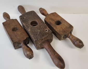 May include: Three antique wooden tools with handles. Each tool has a rectangular body with a central hole and a threaded insert. The tools are made of dark brown wood and show signs of wear.