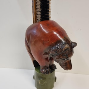May include: A vintage bear-shaped brush holder. The brown wooden bear is mounted on a green base. A brush with a wooden handle and black bristles is inserted into the bear's back. The bear is carved with detailed features.