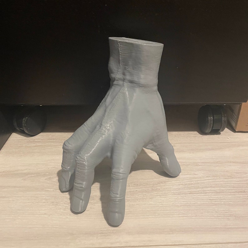 May include: A 3D printed gray hand sculpture with five fingers. The hand is posed with the fingers spread out and the palm facing up.