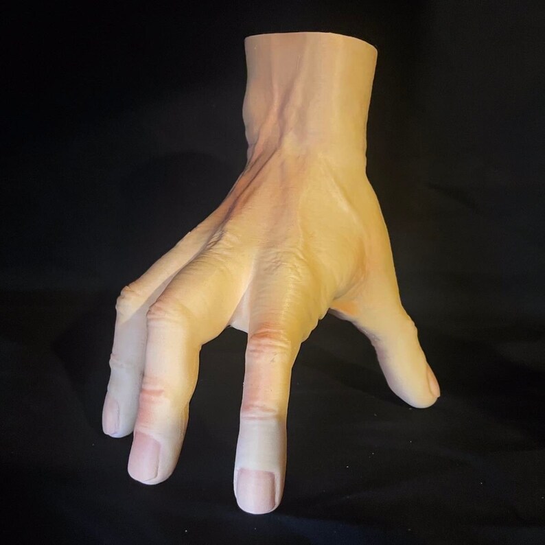 May include: A realistic-looking, flesh-toned, sculpted hand with four fingers extended and one finger curled. The hand is posed as if reaching out or grabbing something.
