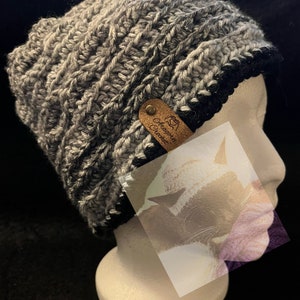 May include: Gray and black crocheted beanie with a brown leather tag that says "Handmade Crochet".