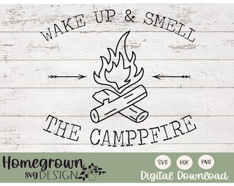 May include: Black and white line art design of a campfire with the text "WAKE UP & SMELL THE CAMPPFIRE" around it. The design is on a white wood background.