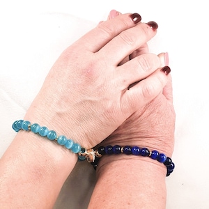 May include: Two bracelets on a person's wrists. The bracelet on the left wrist is made of light blue beads. The bracelet on the right wrist is made of dark blue beads.