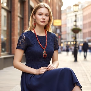 May include: A navy blue dress featuring a lace bodice with short sleeves and a solid skirt. The ensemble is accessorized with a long necklace composed of red beads and a decorative pendant, along with matching red beaded drop earrings.