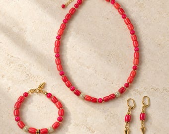 May include: A jewelry set consisting of a necklace, a bracelet, and a pair of drop earrings. The pieces feature cylindrical and spherical red and pink beads, gold-toned metal accents, and small pave-set crystal spheres. The earrings have a pointed gold-toned charm.