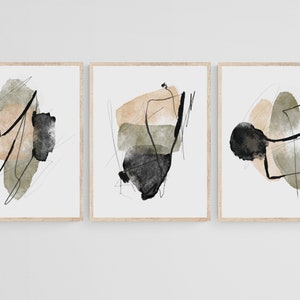 May include: Set of three abstract art prints with black, beige, and green watercolor shapes. The prints are framed in a light wood frame.