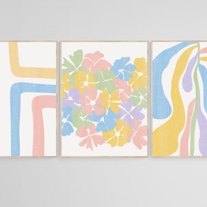 May include: Three abstract art prints with a pastel color palette. The first print features a series of curved lines in shades of green, blue, and pink. The second print features a cluster of stylized flowers in shades of yellow, pink, blue, and green. The third print features a series of wavy lines in shades of yellow, blue, and purple.