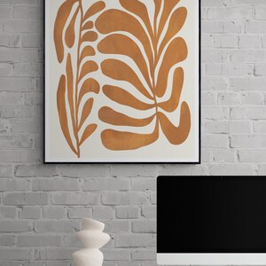 以下が含まれることがあります： 白い背景に茶色の葉の模様が描かれた抽象的なデザインの額装されたプリント
