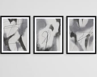 May include: A set of three abstract art prints in black frames. Each print features a grey and white background with black lines and shapes.