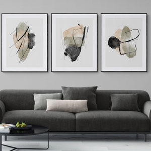 May include: Three framed abstract art prints with black frames. The prints feature abstract shapes in shades of beige, green, and black on a white background.