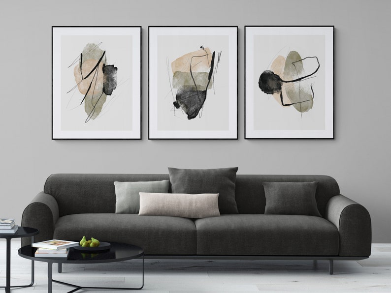 May include: Three framed abstract art prints with black frames. The prints feature abstract shapes in shades of beige, green, and black on a white background.