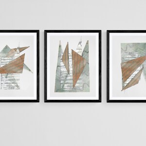 Op de afbeelding: Drie ingelijste abstracte kunstprints met geometrische vormen in tinten van bruin, grijs en wit. De prints zijn geplaatst tegen een witte muur.