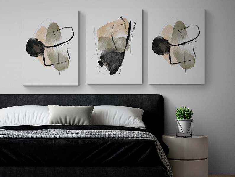 May include: Three abstract art prints with black, brown, and green shapes on a white background. The prints are hanging on a white wall above a black headboard and a bed with a black and white patterned blanket.