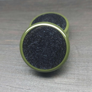 May include: A pair of green and black ear gauges with a speckled black center. The gauges are made of resin and have a smooth, polished finish.