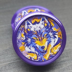May include: Purple and gold round earrings with a wolf face design. The wolf has a white and blue fur pattern with yellow eyes.