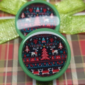 May include: Two green round ornaments with a Christmas sweater design. The design features a red and white snowflake pattern with a green Christmas tree and reindeer.