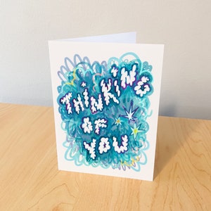 May include: A white card with blue and purple abstract designs and the text "Thinking of You" in white letters.
