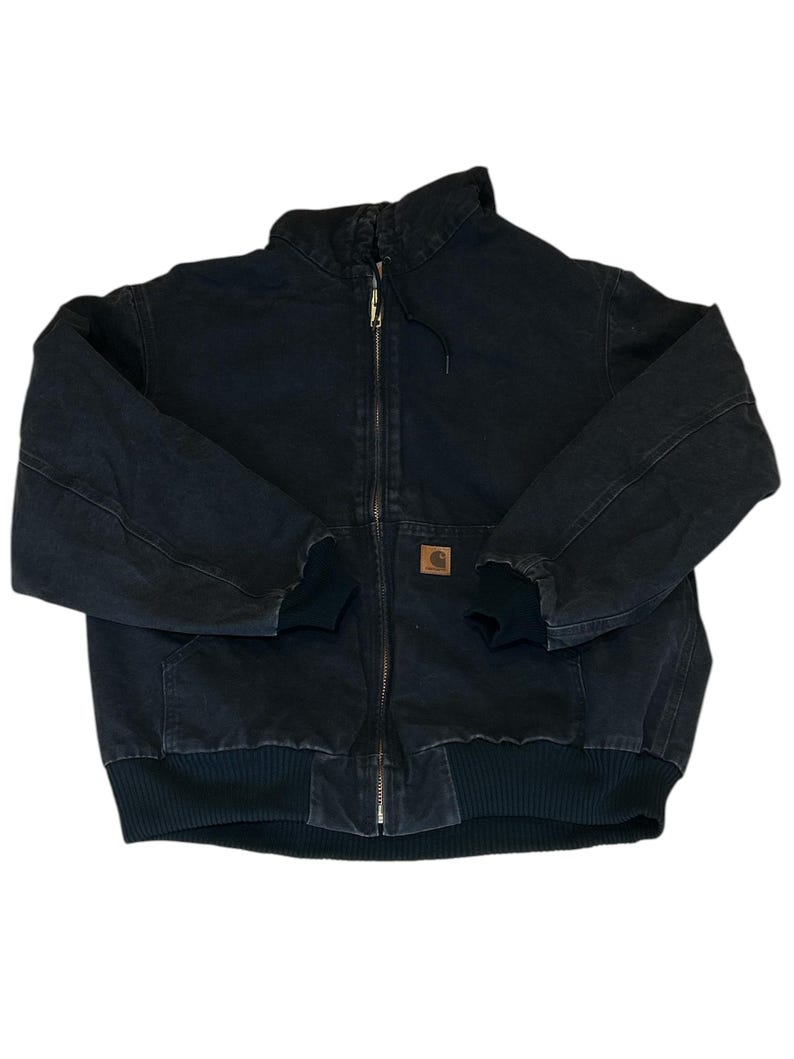 May include: Black work jacket with a full zipper closure, ribbed cuffs, and a ribbed hem. The jacket features a brown square logo patch on the front and a high collar. The jacket is made of a durable, heavy-duty fabric.