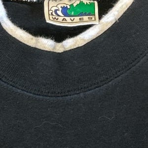 May include: Black sweatshirt with a white ribbed collar and a green and white label that says "WAVES" in all caps.