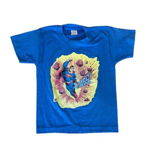 May include: A blue t-shirt with a graphic of Superman flying through the air with the word "CRASH!" in a speech bubble.