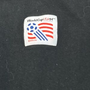 May include: Black t-shirt with a white patch featuring a soccer ball and the text "World Cup USA '94".