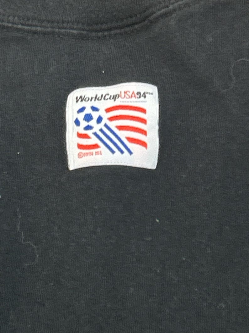 May include: Black t-shirt with a white patch featuring a soccer ball and the text "World Cup USA '94".