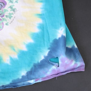 May include: A tie-dye shirt with a blue, purple, and yellow color scheme. The shirt has a small hole in the fabric.