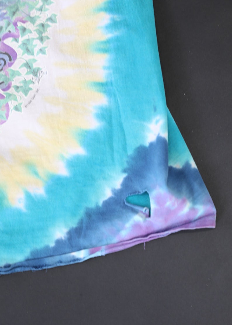 May include: A tie-dye shirt with a blue, purple, and yellow color scheme. The shirt has a small hole in the fabric.