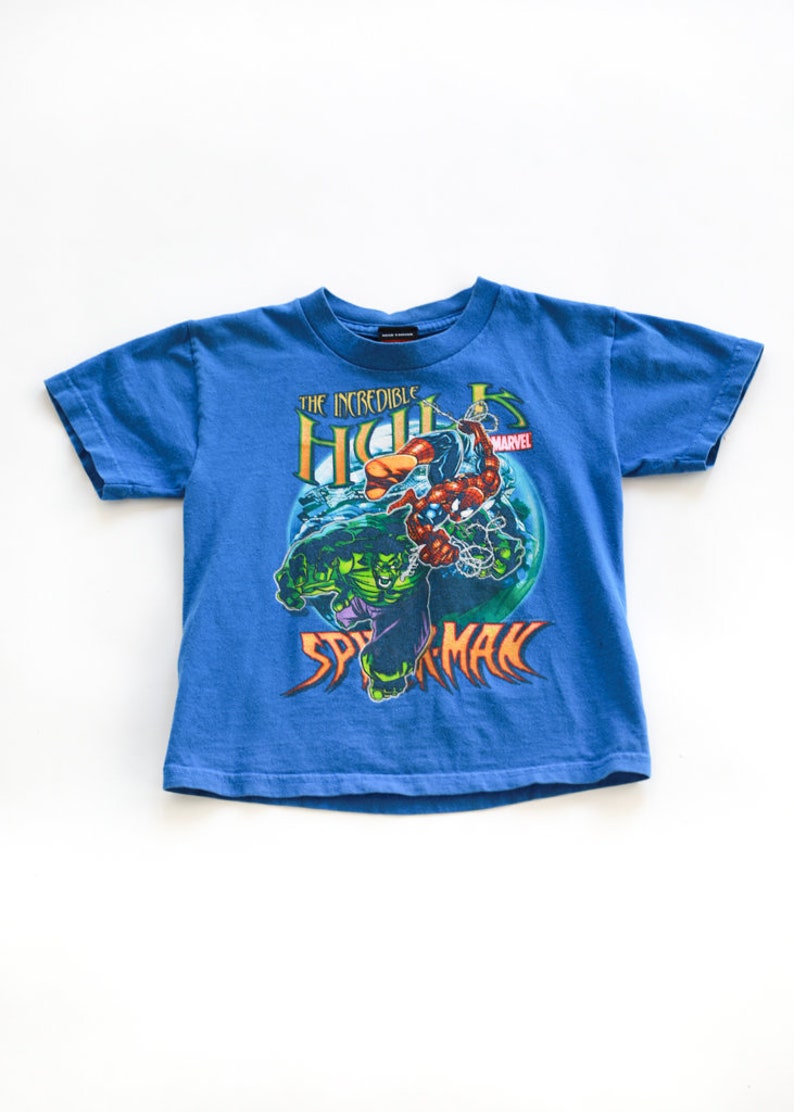 Puede incluir: Una camiseta azul con un estampado gr&aacute;fico de Hulk y Spiderman. El texto "The Incredible Hulk" y "Spiderman" est&aacute; impreso en la camiseta. El logotipo de Marvel tambi&eacute;n est&aacute; impreso en la camiseta.