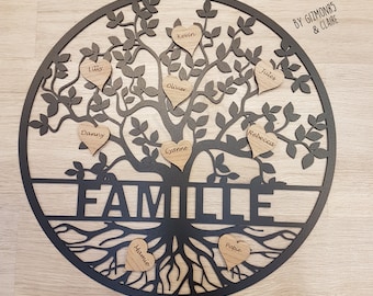 Könnte beinhalten: Schwarze Metall-Wanddekoration in Form eines Familienbaums mit herzförmigen Namensschildern aus Holz. Das Wort "FAMILLE" ist am Baumstamm ausgeschnitten. Das Kunstwerk enthält den Text "CREAZMO" und "BY GIZMONRS & CLAIRE".
