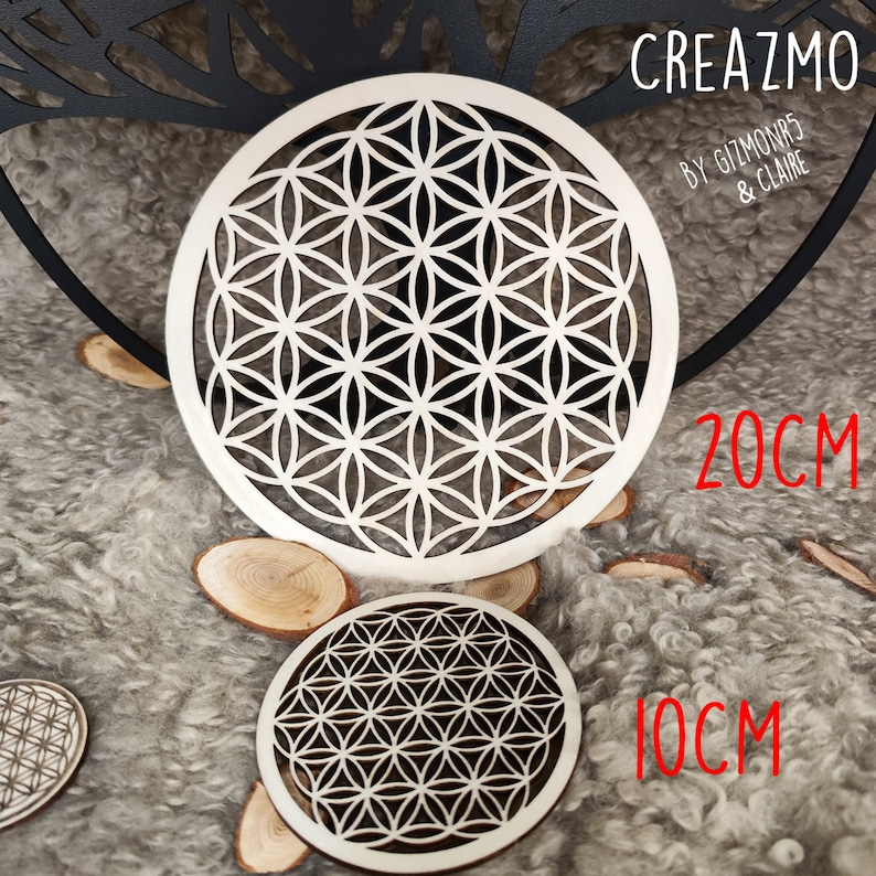 K&ouml;nnte beinhalten: Zwei Holzuntersetzer mit einem geometrischen Blumen des Lebens-Design. Der gr&ouml;&szlig;ere Untersetzer hat einen Durchmesser von 20 cm, der kleinere 10 cm. Die Untersetzer sind hell und liegen auf einer strukturierten, grauen Oberfl&auml;che.
