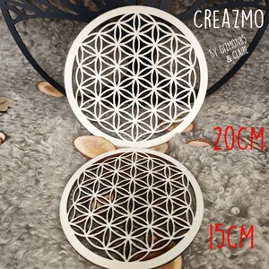 K&ouml;nnte beinhalten: Zwei lasergeschnittene Untersetzer aus Holz mit einem Lebensblumen-Design. Der gr&ouml;&szlig;ere Untersetzer hat einen Durchmesser von 20 cm, der kleinere 15 cm. Die Untersetzer sind aus hellem Holz mit einem geometrischen Muster. Der Text "CREAZMO" ist sichtbar.