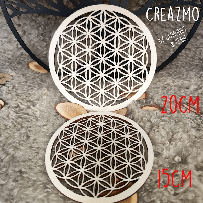 K&ouml;nnte beinhalten: Zwei lasergeschnittene Untersetzer aus Holz mit einem Lebensblumen-Design. Der gr&ouml;&szlig;ere Untersetzer hat einen Durchmesser von 20 cm, der kleinere 15 cm. Die Untersetzer sind aus hellem Holz mit einem geometrischen Muster. Der Text "CREAZMO" ist sichtbar.