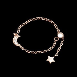 May include: A delicate gold chain ring with a crescent moon charm and a star charm. The ring is adjustable and has a small bead at the end of the chain.