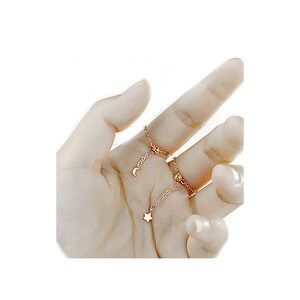 May include: A set of two gold-toned rings with a dangling star and crescent moon charm. The rings are connected by a delicate chain.