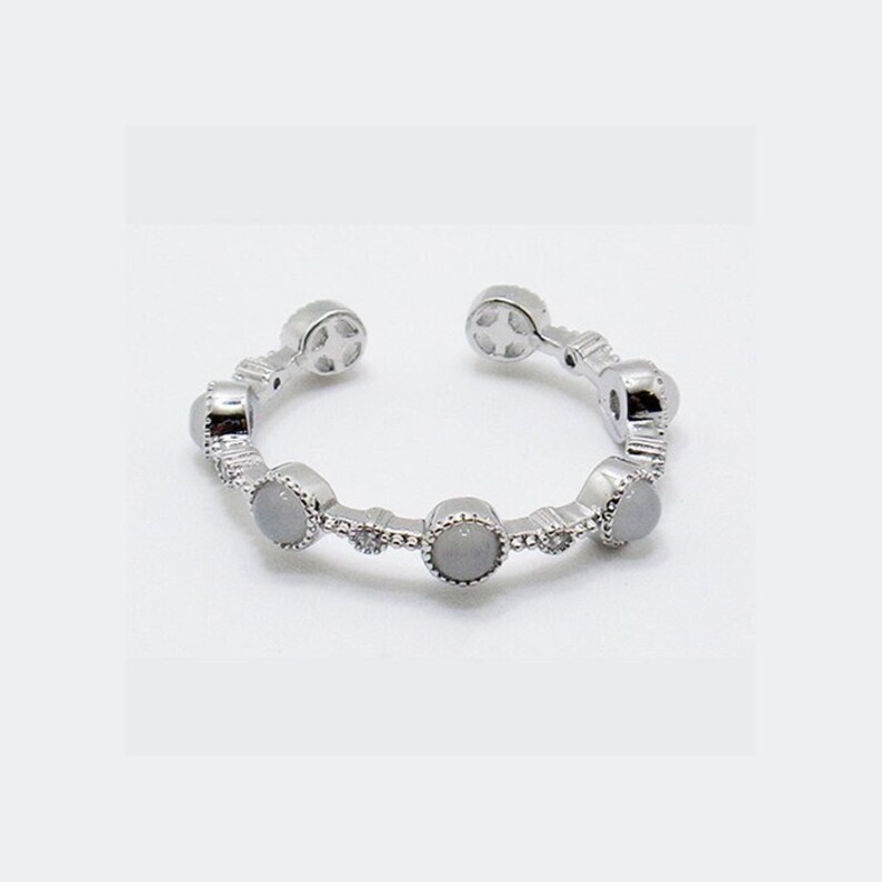 May include: A silver adjustable ring with five white stones set in a silver bezel. Each stone is surrounded by smaller silver accents.