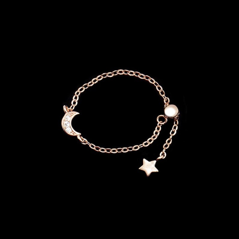 May include: A delicate gold chain ring with a crescent moon charm and a star charm. The ring is adjustable and has a small bead at the end of the chain.