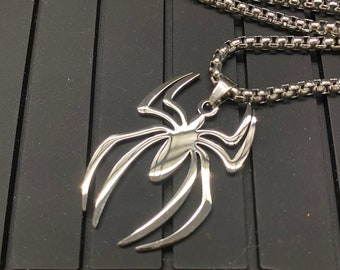 May include: A silver chain necklace with a silver spider pendant. The necklace is on a yellow and black background.