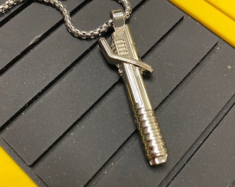 May include: A silver chain necklace with a silver pendant shaped like a tool. The pendant has a textured surface and a small loop at the top.