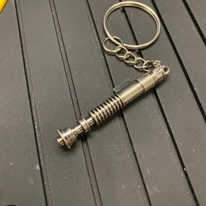 May include: A silver lightsaber keychain with a coiled design and a silver ring.