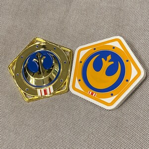 Könnte beinhalten: Zwei Rebel Alliance-Symbol-Anstecker. Einer ist golden mit einem rot-weiß-blauen Streifen. Der andere ist weiß mit einem blau-orange-roten Streifen.