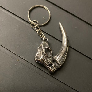 May include: A silver metal dinosaur claw keychain with a skull and a long, curved claw.