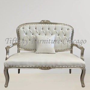 May include: A white loveseat with silver trim and a tufted back. A small white pillow rests on the seat. The furniture has ornate details and curved legs. The text "Tiffany Furniture Chicago" is visible.
